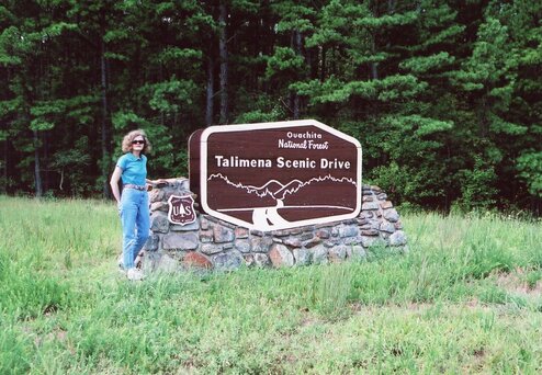 Schall standing in front of large sign:  Ouachita National Forest.  Talimena Scenic Drive.  Tall trees in background.  Oklahoma, 2009. 