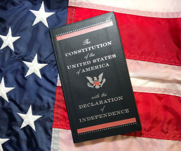Image of front cover of pocket sized book containing the Constitution of the U.S.A. and the Declaration of Independence against a red, white, and blue background